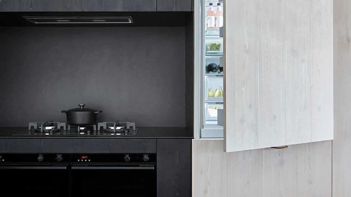Chaudron en céramique noir sur une plaque de cuisson à gaz à côté d’un réfrigérateur ouvert.