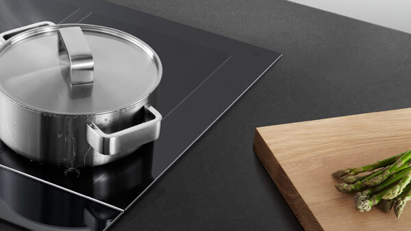 Close up of induction cooktop with a pot and chopping board