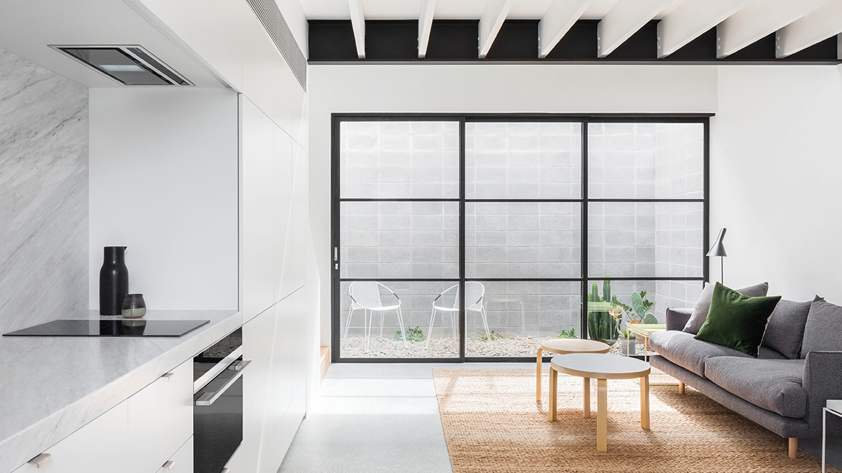 Large white loft with a kitchen to the left looking to a grey concrete courtyard.