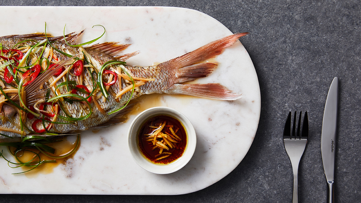 Tail end of a whole cooked snapper garnished with chilli and green herbs.