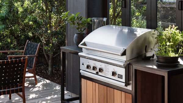 Front View of Outdoor Stainless Steel Grill Countertop atop Wooden Cabinetry Matching Furniture