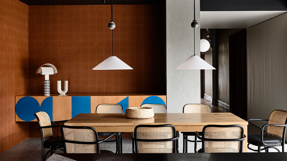 Two pendant lights above an oak dining table with a backdrop of terracotta tiled walls.