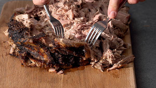 Braised Lamb on a Wooden Block Being Pulled Apart With Two Forks