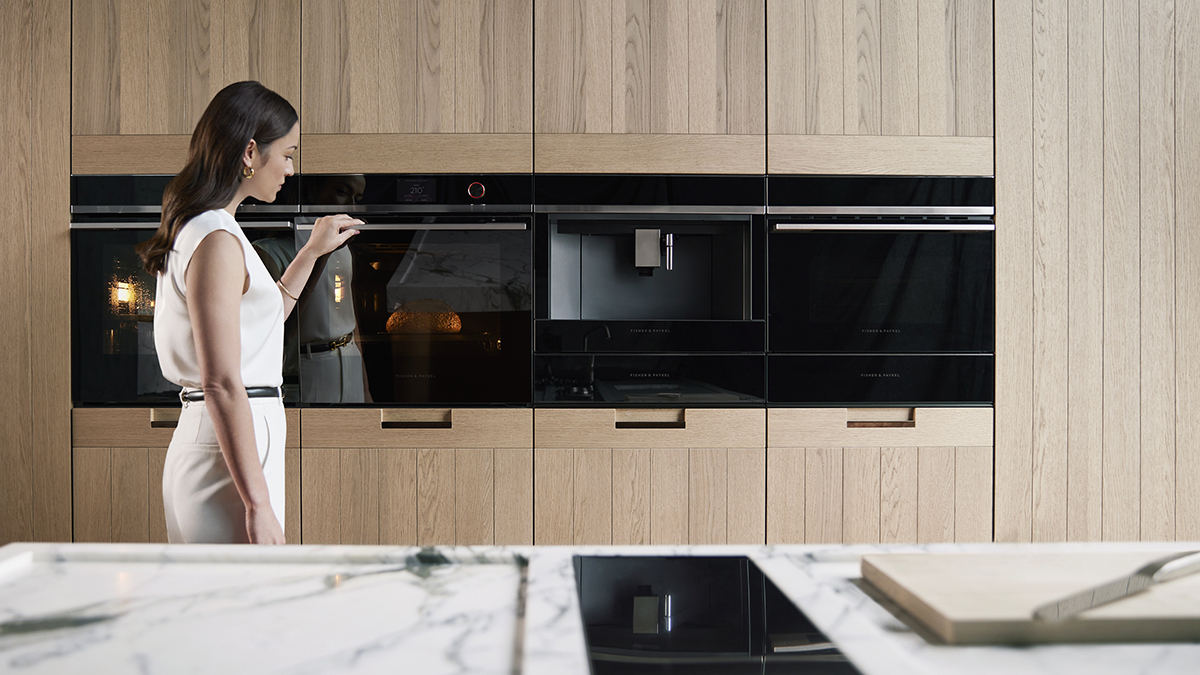 A woman standing next to minimal Fisher & Paykel cooking appliances