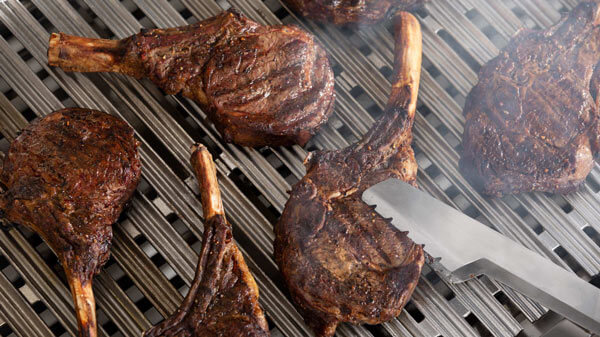 Bone-in Rib-Eye Steaks Being Seared atop a Stainless Steel Grill