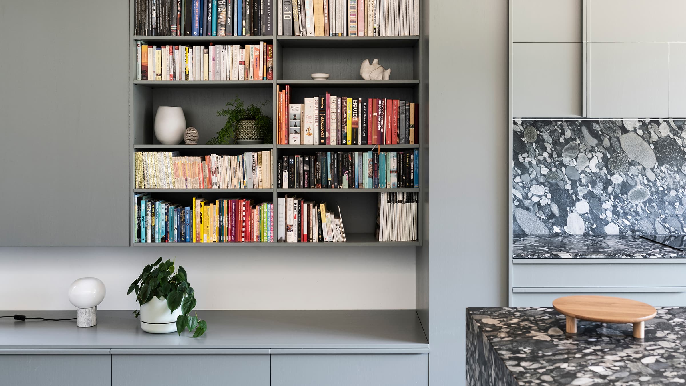 Book shelf organised with some books and show pieces beside the kitchen and dine area