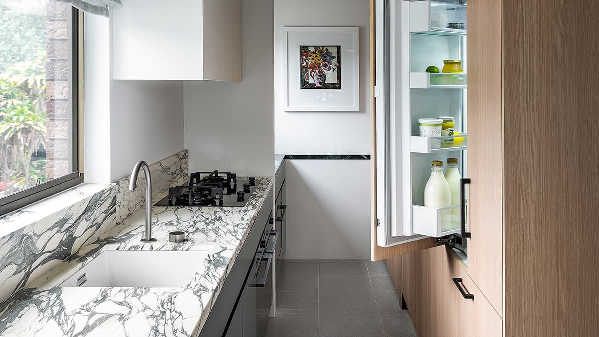 Wide shot of the narrow apartment kitchen with the Integrated French Door Refrigerator ajar.