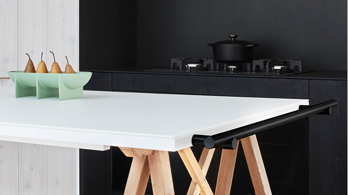 Scandinavian-Style Dining Table with Fruit Bowl and a Black Ceramic Cooking Pot atop a Gas Cooktop in the Foreground.