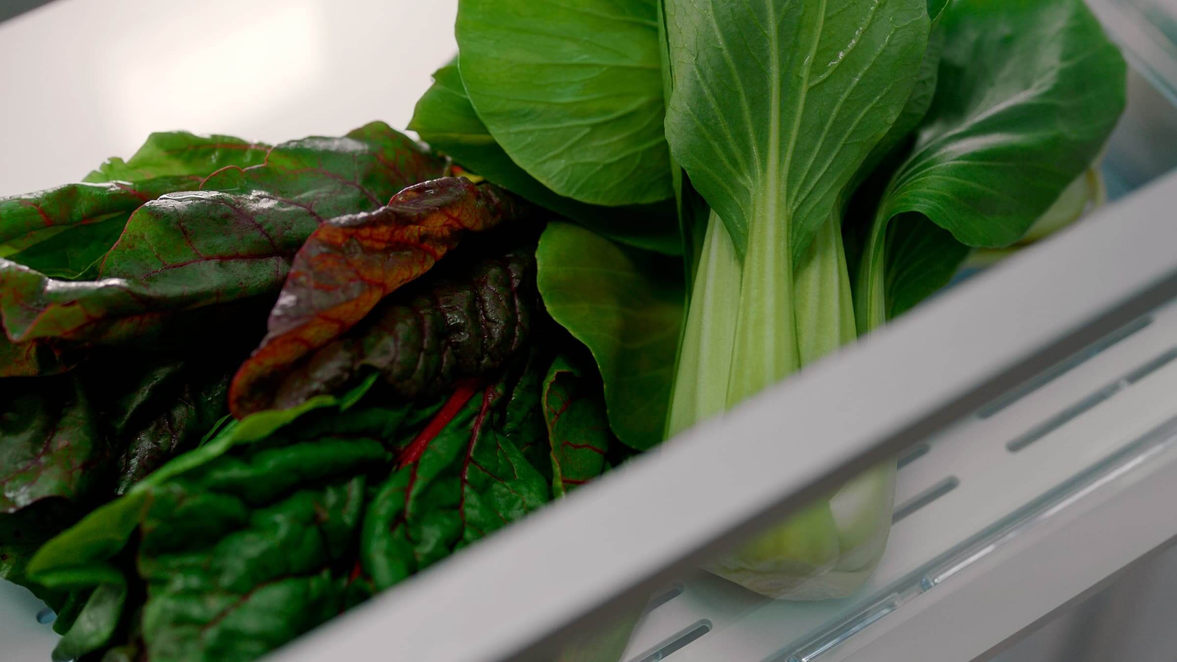 Fresh greens and vegetables stored in a specialized humidity-controlled refrigerator drawer