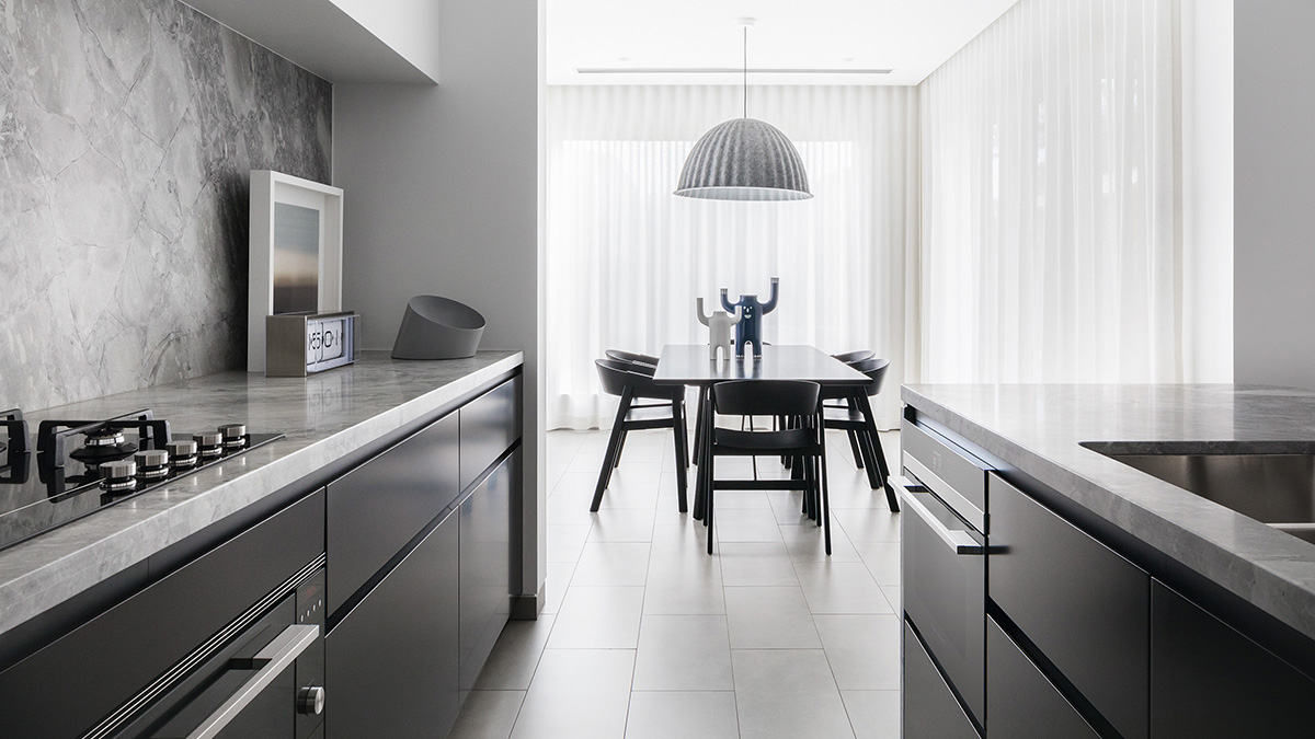 Kitchen with black cabinetry looking through to a black dining table on a backdrop of white floor length curtains.