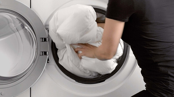 Woman Loading a Thick Duvet Into Washing Machine.