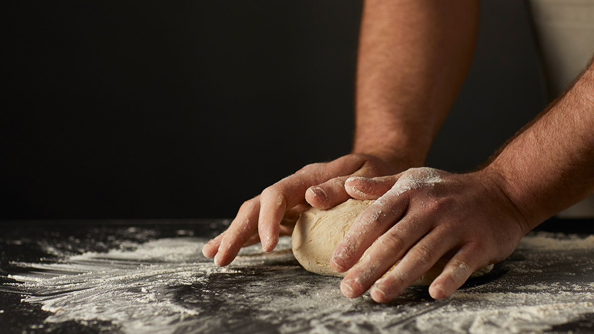 A hand cutting fresh green herbs on a wooden chopping board with stainless steel knife.